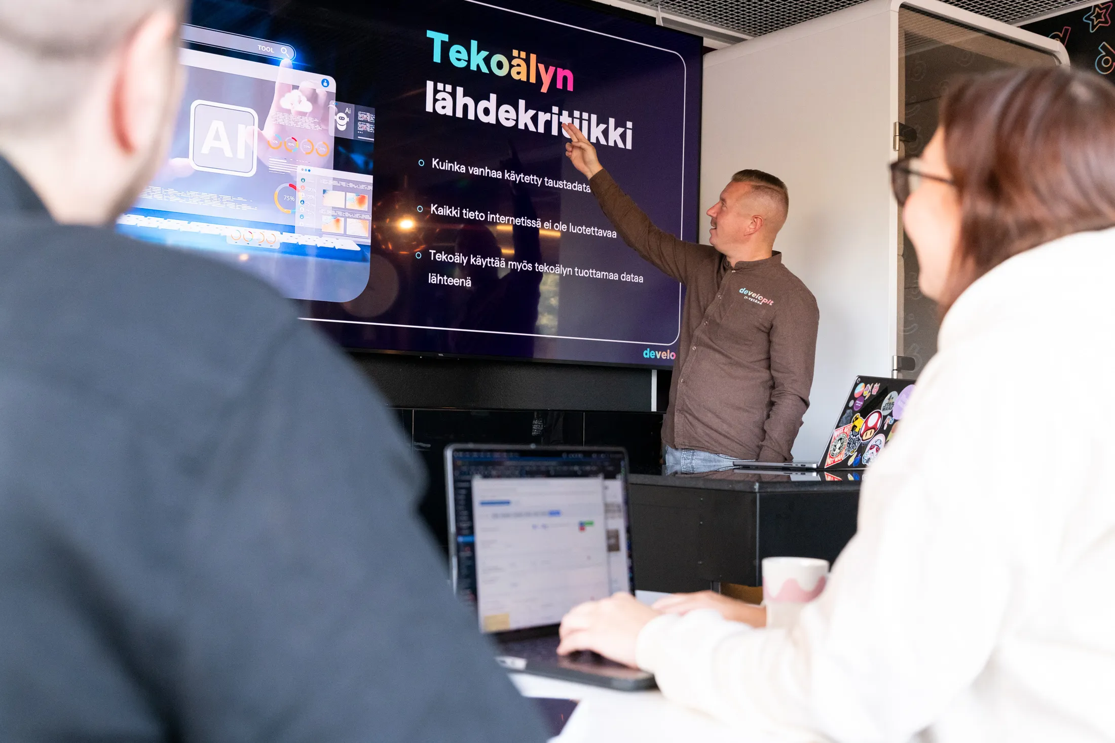 Developitin työntekijä esittelee tekoälyn lähdekritiikkiä käsittelevää diaa yleisölle.