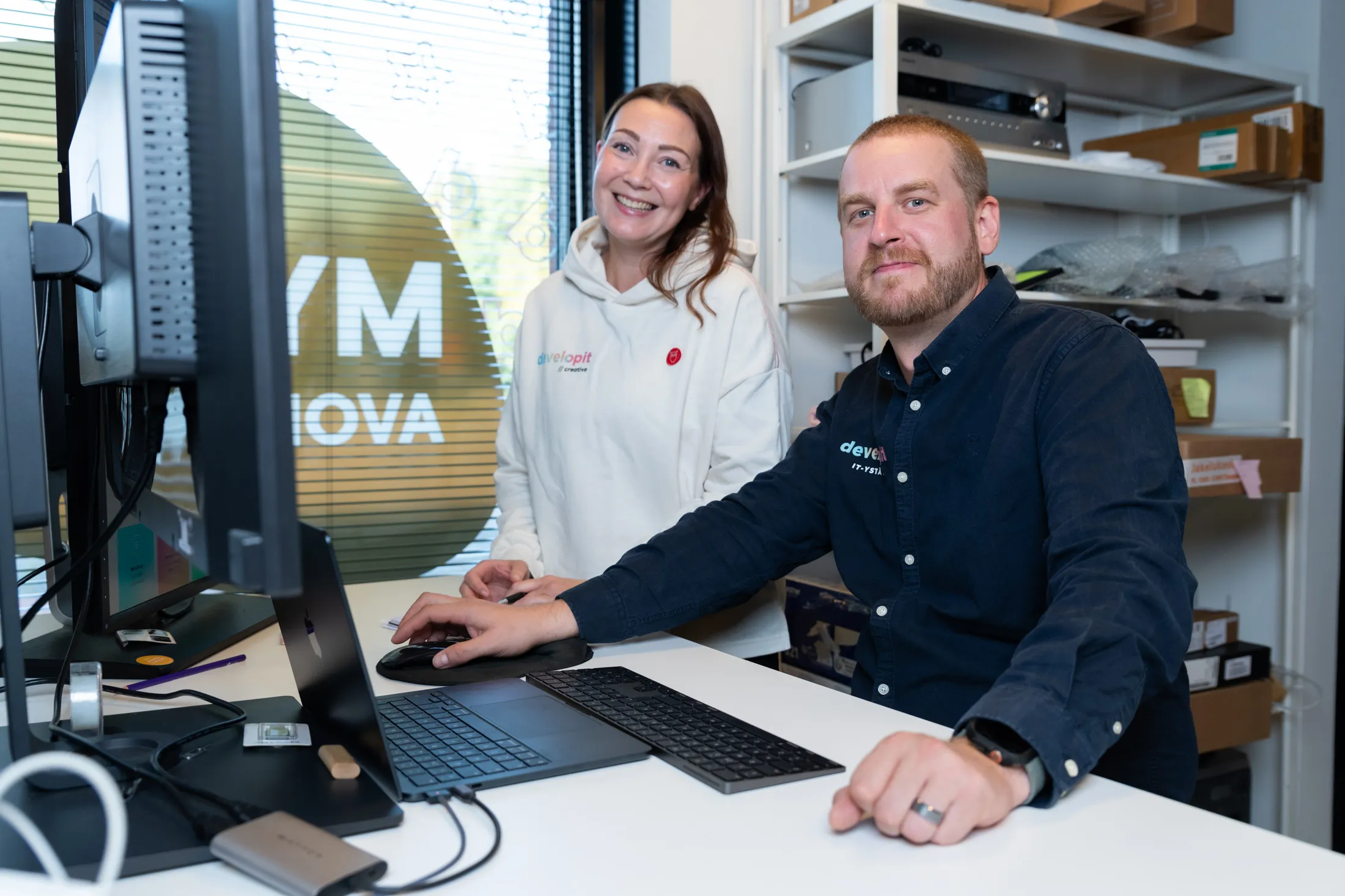 Kaksi Developitin työntekijää järjestelmän näkymien äärellä työpisteellä.